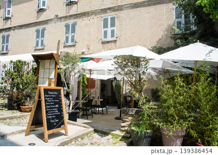 パステルカラーの建物とレストランの店先に置かれたイスとテーブル　地中海のフランス領のコルシカ島にて 139386454