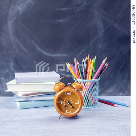School supplies with books, pencils and alarm clock on the table against a blackboard background, back to school concept. School supplies with books, pencils and alarm clock on the table against a blackboard background, back to school concept. 139386465