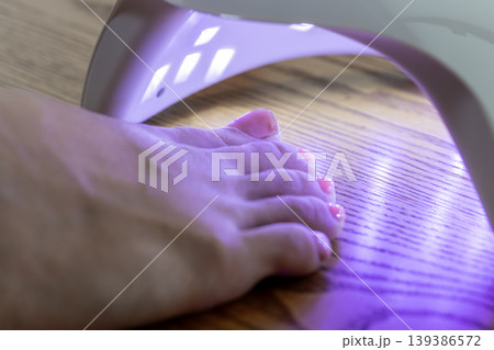足に塗ったジェルネイルにLEDライトを当てているところ 足に塗ったジェルネイルにLEDライトを当てているところ 139386572