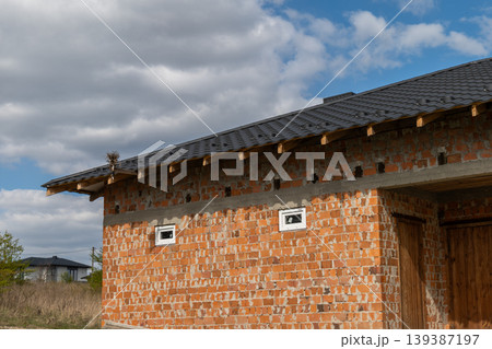House features black metal tiles on the roof and brick walls in a grassy area with trees under a partly cloudy sky 139387197