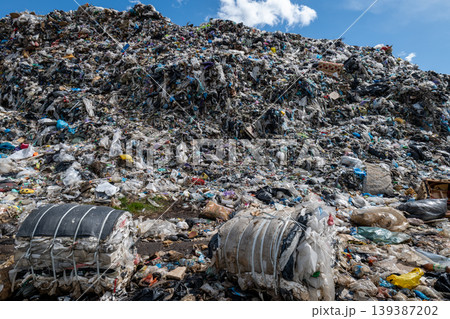 Workers and machines gather waste at a municipal trash site filled with heaps of garbage under a blue sky Workers and machines gather waste at a municipal trash site filled with heaps of garbage under a blue sky 139387202