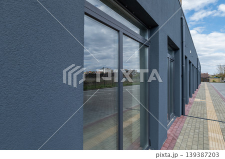 The facade of a new building shows large windows and a nearby parking area with a few clouds in the sky The facade of a new building shows large windows and a nearby parking area with a few clouds in the sky 139387203