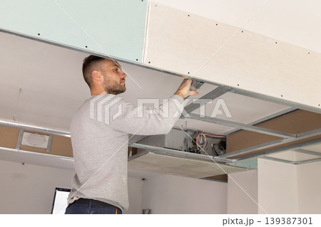 Construction worker installs metal profile frame for drywall suspended ceiling system in apartment 139387301