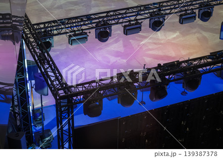 Overhead stage lighting and truss system with spotlights casting purple blue washes for concert event production 139387378