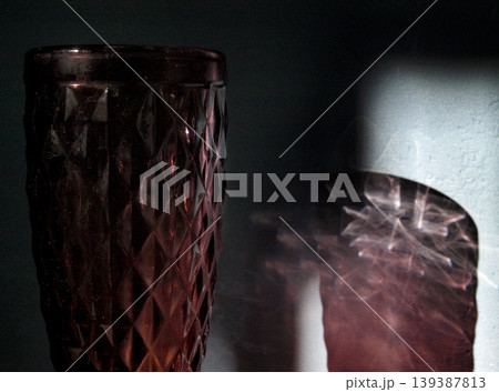 Vertical minimalist photograph exploring the philosophy of existence through a glass and its dramatic shadow. The composition features intricate light caustics and sharp refraction patterns on a plain Vertical minimalist photograph exploring the philosophy of existence through a glass and its dramatic shadow. The composition features intricate light caustics and sharp refraction patterns on a plain 139387813