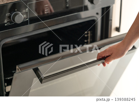 A hand open the door of a modern built-in oven. Concept of home cooking and appliance use. A hand open the door of a modern built-in oven. Concept of home cooking and appliance use. 139388245
