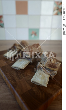 Chunks of raw beef bones displayed on a wooden cutting board with a colorful tiled background in a kitchen setting Chunks of raw beef bones displayed on a wooden cutting board with a colorful tiled background in a kitchen setting 139389188