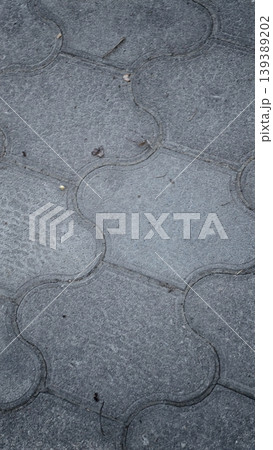 Gray interlocking pavement tiles with a textured surface and subtle imperfections, creating a uniform pattern on the ground in an outdoor setting 139389202