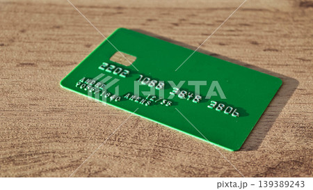 Green credit card with embossed numbers and name displayed on a wooden surface, showcasing the card's design and texture in a close-up view 139389243