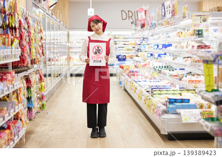 スーパーマーケットの商品の前で万引き防止のプラカードを持つ若い女性 スーパーマーケットの商品の前で万引き防止のプラカードを持つ若い女性 139389423
