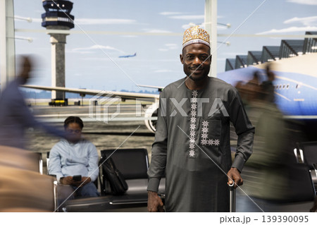 Walking, ethnic clothes and smiling man in airport international transport hub surrounded by blurry silhouettes of people. Rushing, crowd and happy African person in flight departure terminal Walking, ethnic clothes and smiling man in airport international transport hub surrounded by blurry silhouettes of people. Rushing, crowd and happy African person in flight departure terminal 139390095