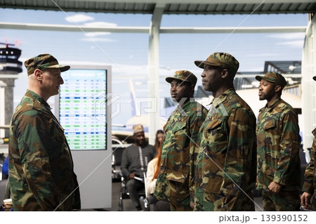 Military troops team receiving orders from veteran in airport terminal, standing in formation. Multiracial army squad wearing camouflage uniforms standing at attention in airport hub Military troops team receiving orders from veteran in airport terminal, standing in formation. Multiracial army squad wearing camouflage uniforms standing at attention in airport hub 139390152