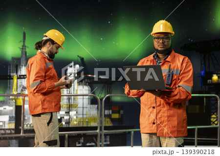 Portrait of industrial drilling boat expert inspecting gear integrity using laptop during aurora borealis. Offshore platform worker does machinery checkup under green northern lights Portrait of industrial drilling boat expert inspecting gear integrity using laptop during aurora borealis. Offshore platform worker does machinery checkup under green northern lights 139390218