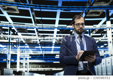 Data center technician using tablet to monitor system performance, identifying bottlenecks. Server farm IT expert using device to implement optimizations improving electronics efficiency Data center technician using tablet to monitor system performance, identifying bottlenecks. Server farm IT expert using device to implement optimizations improving electronics efficiency 139390352