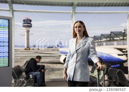 Woman passenger portrait, carrying luggage for business trip, at boarding gate, walking around the airport terminal before departure. Female traveler checking flights information on screens. Woman passenger portrait, carrying luggage for business trip, at boarding gate, walking around the airport terminal before departure. Female traveler checking flights information on screens. 139390507