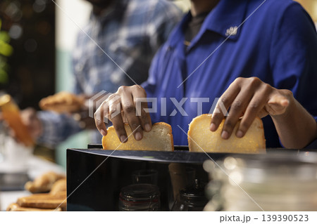 Close up of young black couple preparing bread in a toaster for breakfast table, enjoying toast, homemade pastry and morning coffee. Man and woman showing love and joy in a cozy kitchen. Close up of young black couple preparing bread in a toaster for breakfast table, enjoying toast, homemade pastry and morning coffee. Man and woman showing love and joy in a cozy kitchen. 139390523