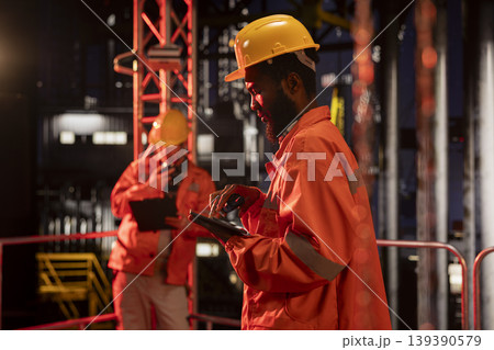 African american engineer exchanges insights on walkie talkie from drilling platform, coordinating fuel and natural petroleum extraction on offshore oil rig. Efficient fossil fuels production. 139390579