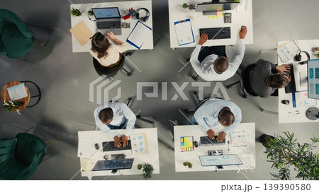 Top down view of business people gathered around laptops working on project tasks for development. Office environment promotes synergy, teamwork and insight through analytics. Top down view of business people gathered around laptops working on project tasks for development. Office environment promotes synergy, teamwork and insight through analytics. 139390580