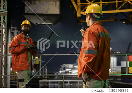 Worker communicating via radio stations on offshore oil platform late at night, managing drilling rig systems to ensure efficient petrol extraction from maritime habitat. Oil industry. 139390581