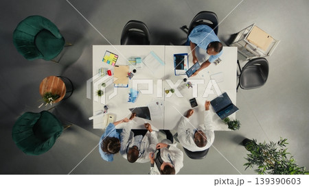 Top down view of medical specialists participating in a clinical discussion on diagnosis and treatment. Doctors and nurses analyze healthcare data and coordinate strategies. 139390603