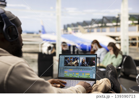 Black videographer reviewing film montage and editing in post production, seated in airport lounge before boarding. International travel with nomadic lifestyle, work anywhere concept. Black videographer reviewing film montage and editing in post production, seated in airport lounge before boarding. International travel with nomadic lifestyle, work anywhere concept. 139390713