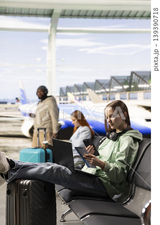 Digital nomad scanning plane ticket on smartphone in international airport, working online as people pass by with suitcases. Nomadic lifestyle emphasizes freedom and global mobility. 139390718