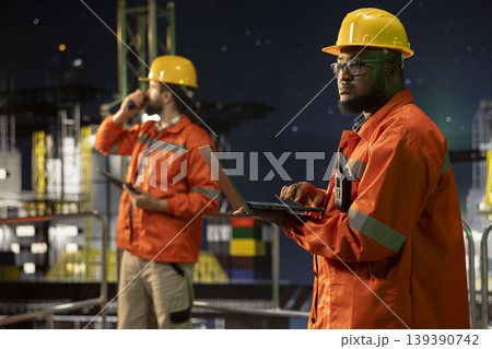 Offshore fossil fuel platform engineering team analyze extraction efficiency during 24 hour operation. African american man on drilling barge and colleague configuring vessel systems Offshore fossil fuel platform engineering team analyze extraction efficiency during 24 hour operation. African american man on drilling barge and colleague configuring vessel systems 139390742