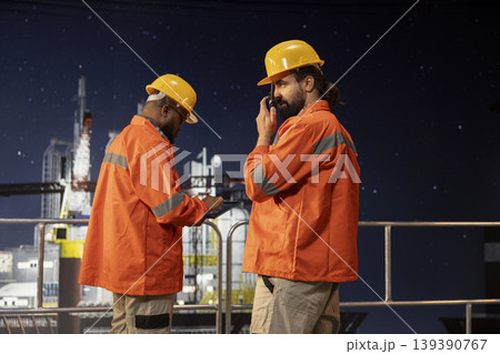 Drilling barge engineer using two way radio to coordinate emergency response procedures. Offshore platform worker facilitating quick communication with technical team during late shift operations 139390767