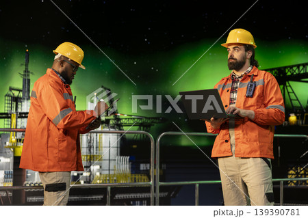 Industrial drilling ship workers inspect equipment integrity using laptop during aurora borealis. Offshore platform colleagues performing machinery checkup to ensure safety under arctic lights Industrial drilling ship workers inspect equipment integrity using laptop during aurora borealis. Offshore platform colleagues performing machinery checkup to ensure safety under arctic lights 139390781