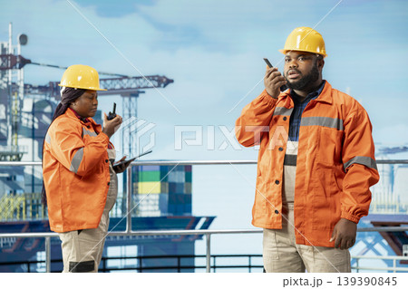 Drilling rig engineering team uses two way radio to communicate with logistics crew. Offshore platform teamworking colleagues speak in walkie talkie providing audio clarity in noisy environment Drilling rig engineering team uses two way radio to communicate with logistics crew. Offshore platform teamworking colleagues speak in walkie talkie providing audio clarity in noisy environment 139390845