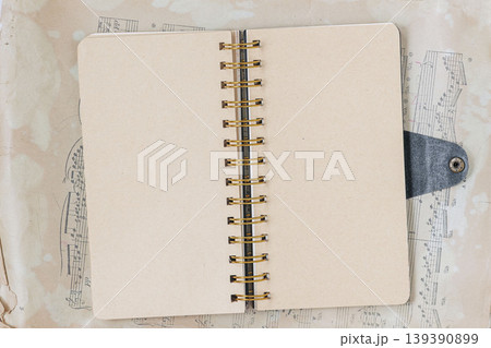 Flat lay of open notebook with spiral binding lies on sheet music, with blank pages ready for notebook layout, writing, journaling, study, or planner mockup. Concept of education, music, design Flat lay of open notebook with spiral binding lies on sheet music, with blank pages ready for notebook layout, writing, journaling, study, or planner mockup. Concept of education, music, design 139390899