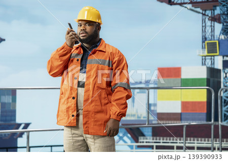 Man on offshore barge deck using portable radio for continuous communication with coworkers. Drilling rig professional speaks in walkie talkie, coordinating with team colleagues 139390933
