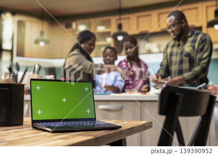 Chroma key screen next to african American family enjoying pizza day in kitchen, laughing as they roll dough and add veggies. Domestic activity shows the happiness of family bonding. 139390952