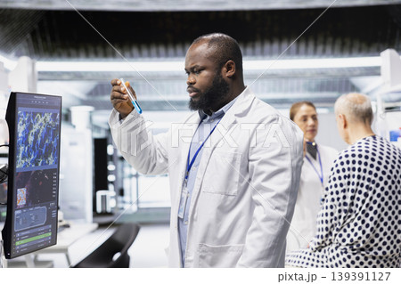 African american researcher monitoring chemical reaction of matter in test tube, working on RD strategy in laboratory and conducting a biotechnology clinical trial with a patient. African american researcher monitoring chemical reaction of matter in test tube, working on RD strategy in laboratory and conducting a biotechnology clinical trial with a patient. 139391127
