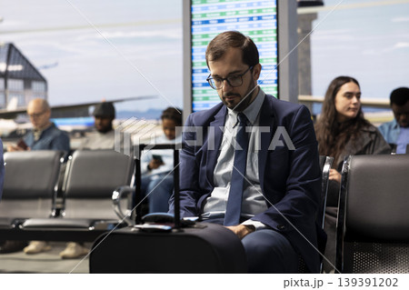 Freelancer in airport terminal lounge working on laptop while traveling to international conference. Telecommuting businessman finishing tasks on notebook device, concept of delayed flight 139391202