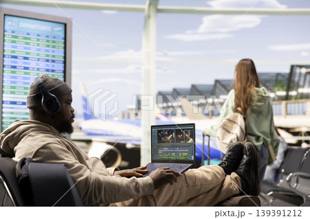 Independent filmmaker editing cinematic video footage on laptop in airport terminal lounge, mixing transitions and visual effects for online production. Remote working and digital nomad job. 139391212