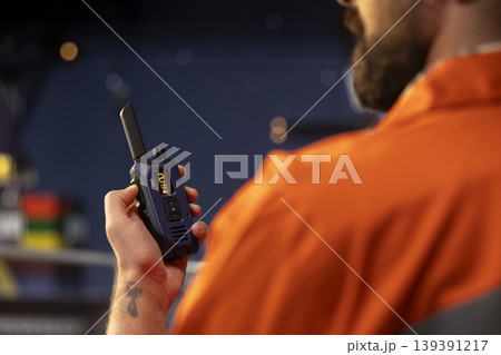 Close up of drilling barge technician using two way radio to coordinate emergency response procedures. Offshore platform employee communicating with technical team during night shift 139391217