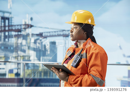 Woman working for industrial offshore rig monitoring operations on oil platform deck using tablet. African american drilling rig employee reviewing energy operations using device 139391276