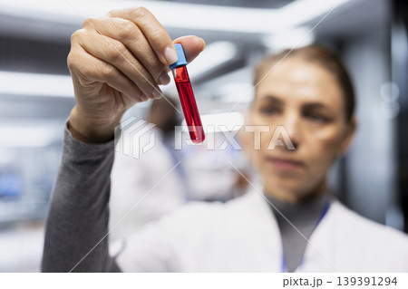 Female researcher examining blood in test tubes during treatment testing, doing a drug study and monitoring a patient. Evaluating pharmacology data for healthcare progress and innovation. 139391294