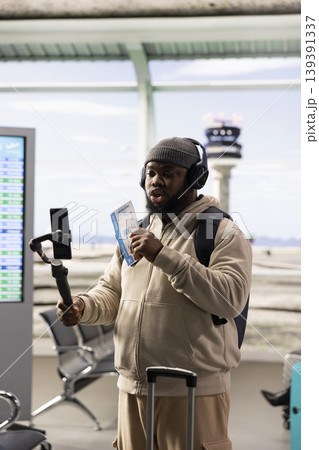 African american vlogger capturing travel moments on smartphone in busy airport terminal, recording video content for social media channel. Influencer lifestyle and digital communication. 139391337