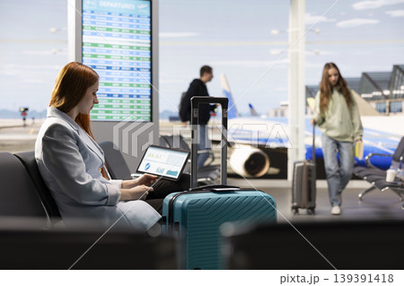 Digital nomad woman checking business data and digital marketing insights on laptop in the airport waiting area, remote work conditions. Work anywhere concept with financial analysis tasks. 139391418