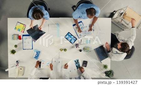 Top down view of doctors participating in a healthcare team meeting to review patient care. The discussion focuses on treatment planning and advancement in modern medicine. Top down view of doctors participating in a healthcare team meeting to review patient care. The discussion focuses on treatment planning and advancement in modern medicine. 139391427