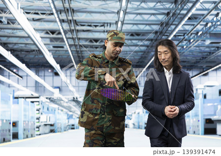 Military man talks with manager about using silicon wafer supply chain for national security purposes. Army officer and management executive reviewing strategic microelectronics factory production Military man talks with manager about using silicon wafer supply chain for national security purposes. Army officer and management executive reviewing strategic microelectronics factory production 139391474