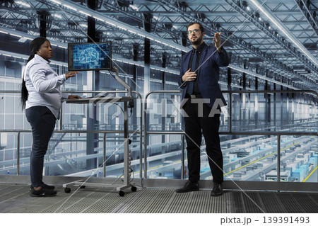 Man and coworker in microchip factory using AI technology to manage resource allocation. Directors analyzing industry 4.0 semiconductor plant operations efficiency using artificial intelligence Man and coworker in microchip factory using AI technology to manage resource allocation. Directors analyzing industry 4.0 semiconductor plant operations efficiency using artificial intelligence 139391493