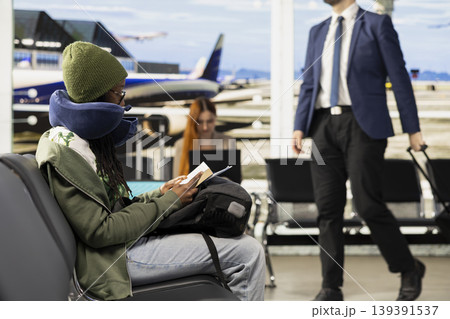 Busy airport departure area with female traveler checking flight schedule, looking at screen and reviewing boarding pass information. Waiting area with passengers preparing for flying. 139391537