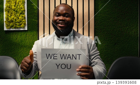 African american HR staff holding paper signs with hiring messages, announcing job openings and inviting skilled candidates to join the company workforce. Workplace culture advertisement. Camera A. 139391608