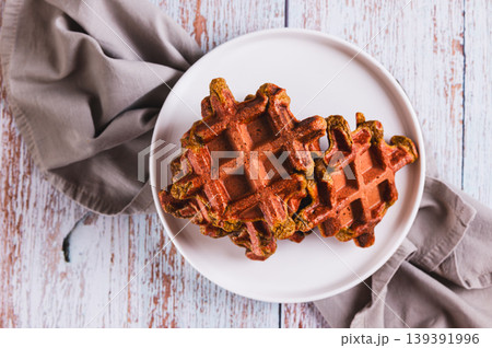 Close up of savory delicious beetroot waffles on a plate on the table top view Close up of savory delicious beetroot waffles on a plate on the table top view 139391996