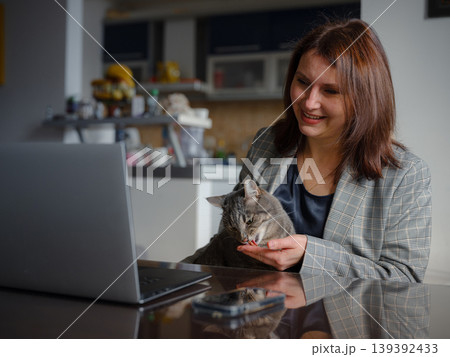 Mother working remotely from home, caucasian woman with her cat using laptop at home. Smart working and smart studying with pet Mother working remotely from home, caucasian woman with her cat using laptop at home. Smart working and smart studying with pet 139392433