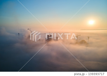Aerial view of cement factory with high concrete plant structure and tower crane at industrial manufacturing site on foggy evening. Production and global industry concept. 139393717