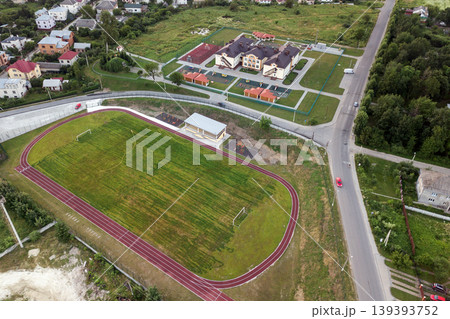 Aerial view of a football field on a stadium covered with green grass in rural town area. Aerial view of a football field on a stadium covered with green grass in rural town area. 139393752